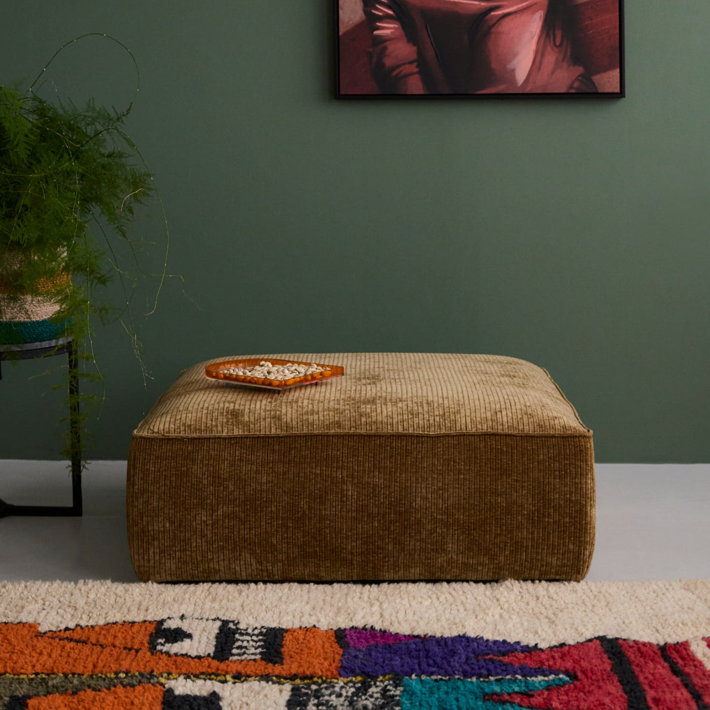 Hocker Nica mit Stoff Breitcord in Farbe goldbraun. Sichtbar ist die quadratische Form mit klaren Kanten und der gleichmäßigen Cordstruktur auf der Oberseite. Das Modell ist mittig platziert und dadurch deutlich zu erkennen.