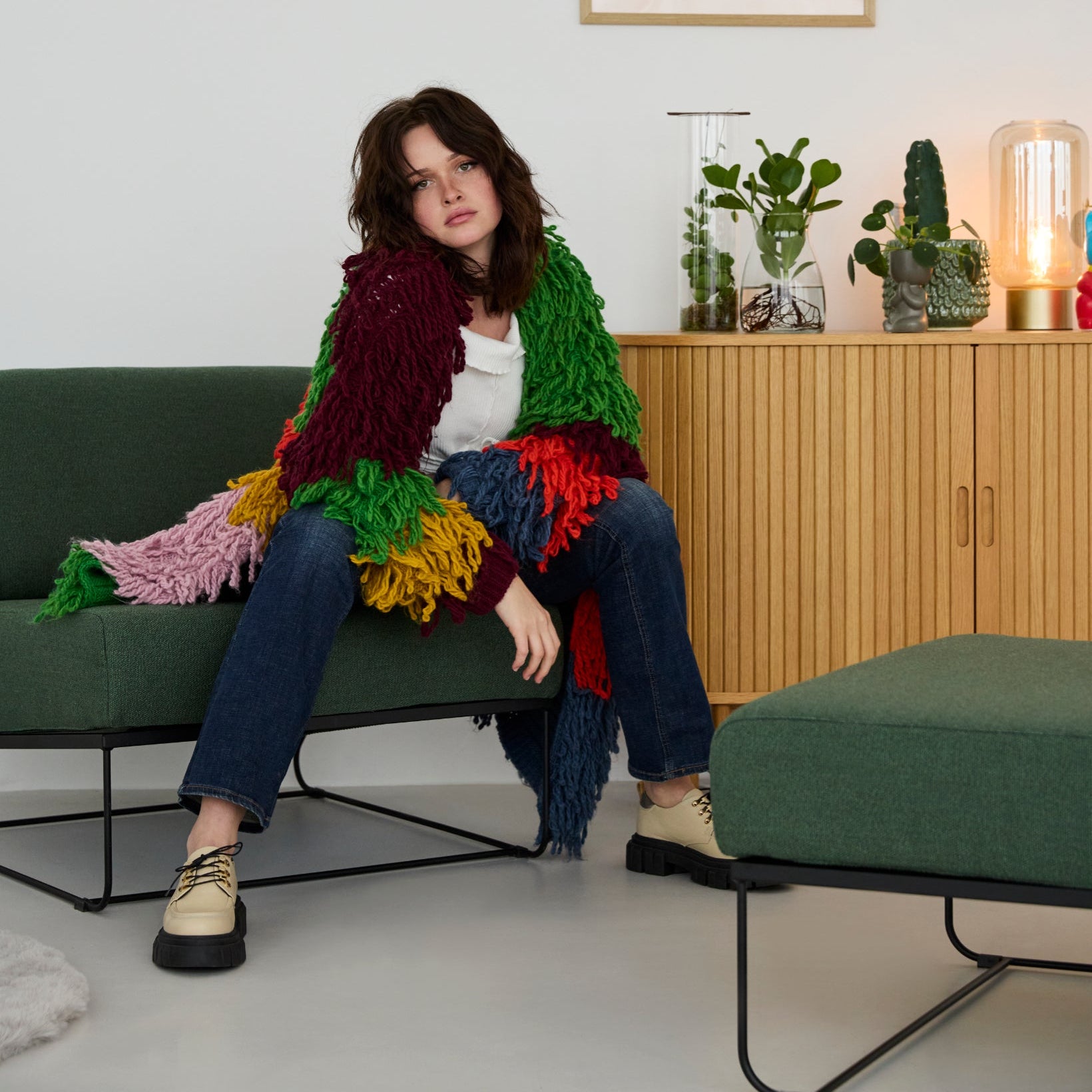 Modulares Sofa Aksel von Yvi Living, bezogen mit dem Stoff Ocean in Grün, in einem modernen Wohnraum. Eine Person sitzt lässig auf dem Aksel-Modul, während im Hintergrund ein Sideboard mit Pflanzen und einer Lampe steht. An der Wand hängt ein Poster mit der Aufschrift „Creative Mode“. Der Fokus liegt klar auf dem Aksel Sofa im Stoff Ocean Grün.