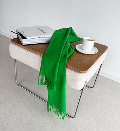 Beistelltisch „Prop!Up“ von Yvi Living mit heller Polsterung und Holzplatte, dekoriert mit grünem Schal, Buch und Kaffeetasse auf hellem Boden.