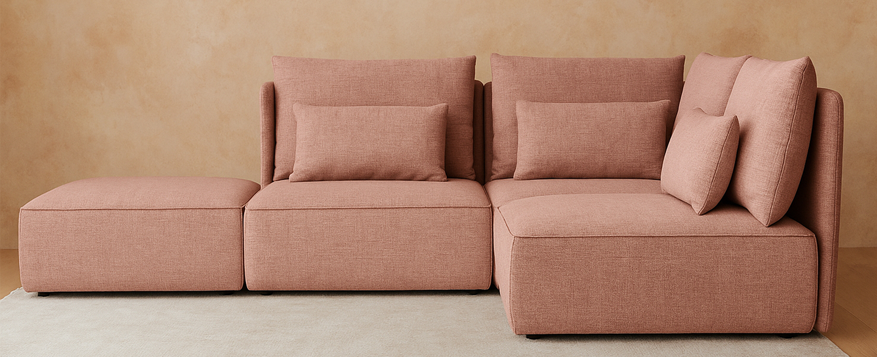 Modulares Sofa NICA in warmem Roséton, bestehend aus zwei Sitzelementen, einem Eckmodul und passendem Hocker – modern inszeniert vor beigefarbener Wand und hellem Teppich. Ideal für flexible Wohnkonzepte mit stilvollem Komfort.