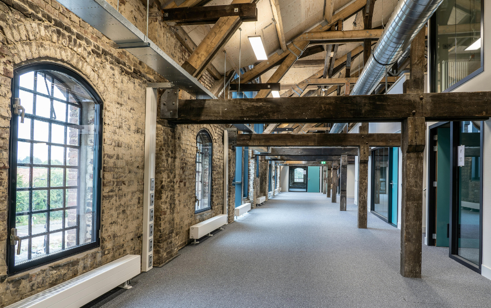 Modern saniertes Bürogebäude im Industrial Style mit offenen Holzbalken, freigelegtem Mauerwerk, großen Rundbogenfenstern und sichtbaren Lüftungsrohren - stilvolle Kombination aus Altbaucharme und moderner Architektur.